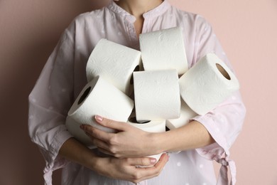 Woman with heap of toilet paper rolls on pink background, closeup