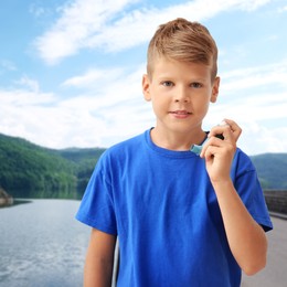 Image of Little boy with asthma inhaler near lake. Emergency first aid during outdoor recreation