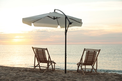 Wooden deck chairs and outdoor umbrella on sandy beach at sunset. Summer vacation