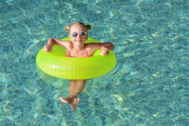 Happy little girl with inflatable ring in outdoor swimming pool on sunny day, space for text