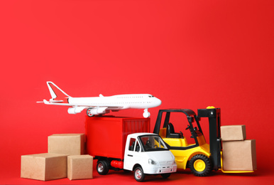 Different toy vehicles with boxes on red background. Logistics and wholesale concept
