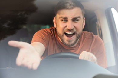 Emotional man in car, view through windshield. Aggressive driving behavior