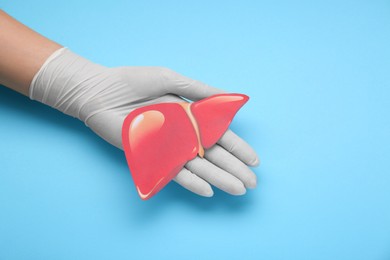 Photo of Doctor in glove holding paper liver on light blue background, closeup and space for text. Hepatitis treatment