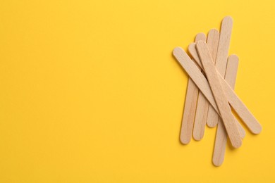 Wooden waxing spatulas on yellow background, flat lay. Space for text