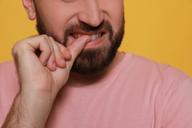 Man biting his nails on yellow background, closeup. Bad habit