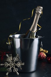 Happy New Year! Bottle of sparkling wine in bucket and festive decor on black background