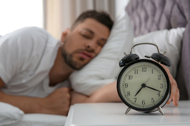 Man sleeping at home in morning, focus on alarm clock