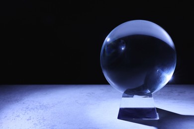 Photo of Crystal prediction ball on table in darkness, space for text. Fortune telling