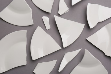 Pieces of broken white ceramic plate on grey background, flat lay