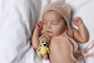 Cute little baby with toy bear sleeping on soft bed, top view