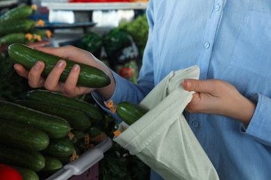 Woman putting cucumber into cotton eco bag at wholesale market, closeup. Life without plastic