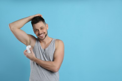 Photo of Handsome man applying deodorant on turquoise background. Space for text