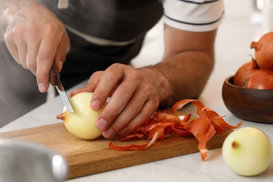Man peeling onion at kitchen counter, closeup. Preparing vegetable