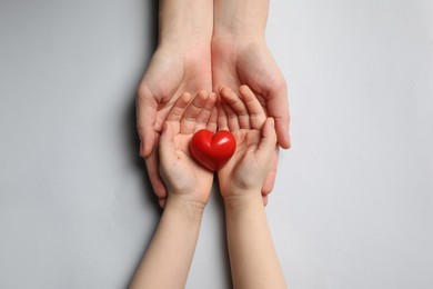 Woman and kid holding red heart in hands on light grey background, top view