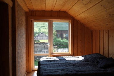 Cozy bedroom with window and wooden walls on sunny day