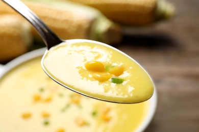 Spoon of delicious corn soup over full bowl, closeup
