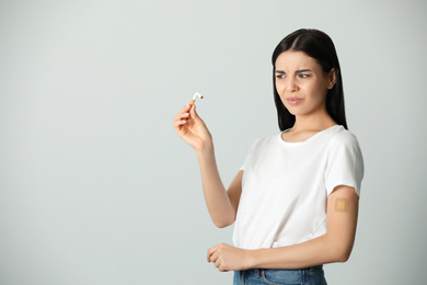 Emotional young woman with nicotine patch and cigarette on light grey background. Space for text