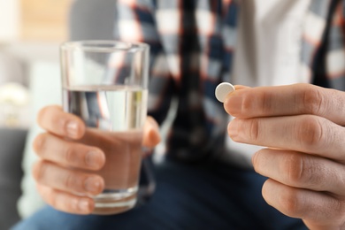 Man holding pill and glass of water indoors, closeup