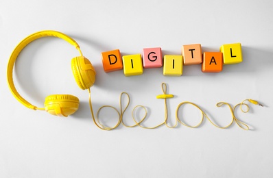 Words DIGITAL DETOX made with colorful cubes and wire of headphones on white background, top view