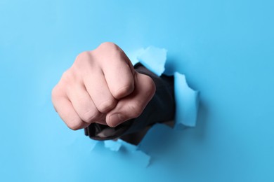 Photo of Businessman breaking through light blue paper with fist, closeup
