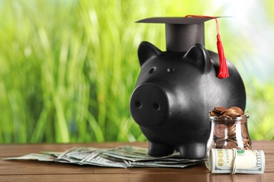 Photo of Scholarship concept. Graduation cap, glass jar with coins, dollar banknotes and piggy bank on wooden table, space for text