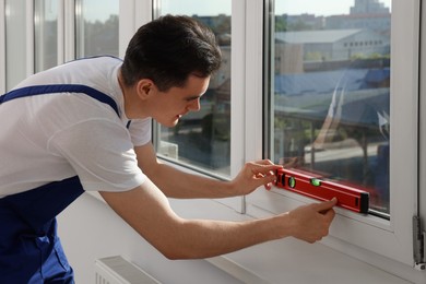 Worker using bubble level after plastic window installation indoors