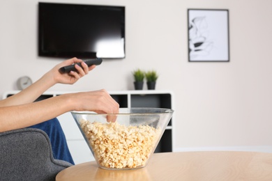 Photo of Young woman watching TV while eating popcorn at home