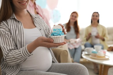 Pregnant woman with cupcake at home during baby shower party, closeup