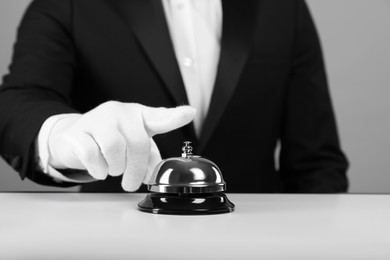 Butler ringing service bell at white table, closeup