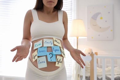 Pregnant woman with different baby names on belly at home, closeup