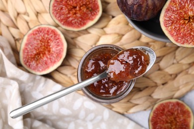 Photo of Glass jar of tasty sweet fig jam with spoon and fruits on table, flat lay