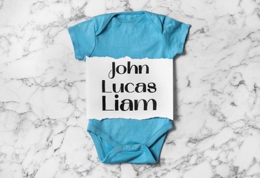 Bodysuit with different baby names on white marble background, top view