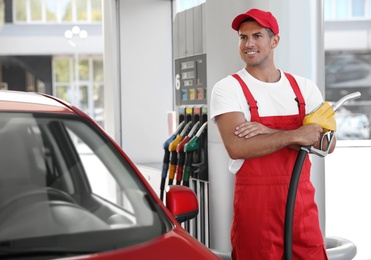 Worker with fuel pump nozzle near car at modern gas station