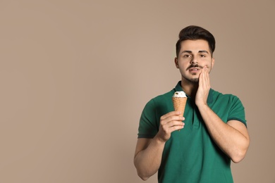 Young man with sensitive teeth and ice cream on color background. Space for text