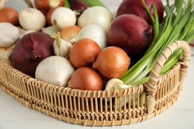 Photo of Wicker tray with fresh onions and garlic on white table, closeup