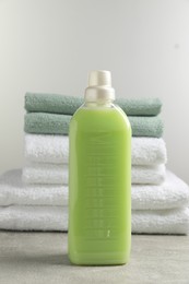 Photo of Bottle of laundry detergent and stacked fresh towels on grey table