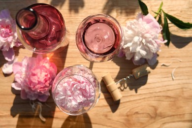 Photo of Bottle and glasses of rose wine near beautiful peonies on wooden table, flat lay