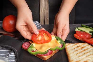 Woman adding tomato to sandwich at grey table, closeup