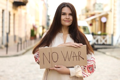 Photo of Smiling woman in embroidered dress holding poster No War on city street