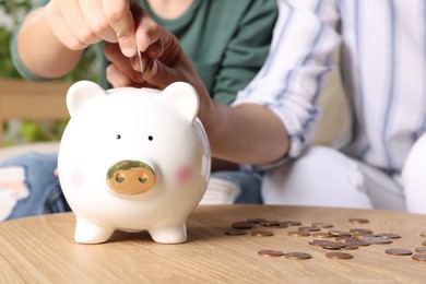 Boy with his mother putting coin into piggy bank at home, closeup