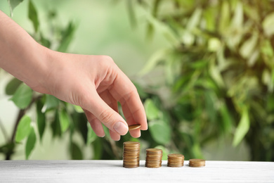 Woman stacking coins on white wooden table against blurred background, closeup. Money savings