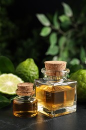 Glass bottles of bergamot essential oil and fresh fruits on black stone table