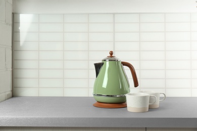 Stylish electric kettle and tea cups on grey table against white wall, space for text