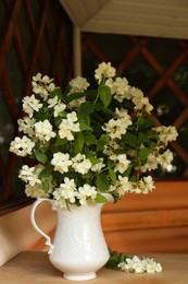 Bouquet of beautiful jasmine flowers in vase on wooden table indoors