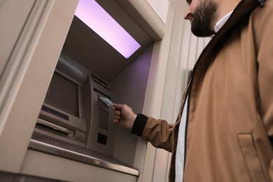 Man inserting credit card into cash machine outdoors, low angle view