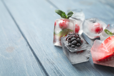 Ice cubes with different berries and mint on blue wooden table, closeup. Space for text