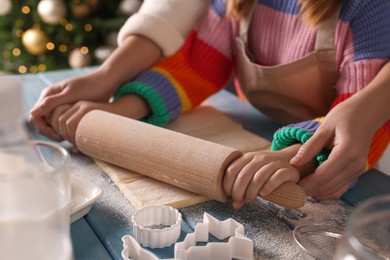 Mother and child rolling dough for Christmas cookies at blue wooden table together, closeup
