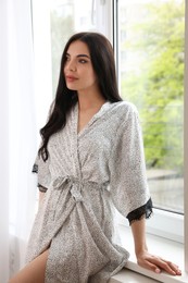 Pretty young woman in beautiful silk robe near window at home