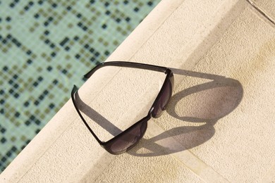 Photo of Stylish sunglasses near outdoor swimming pool on sunny day, above view