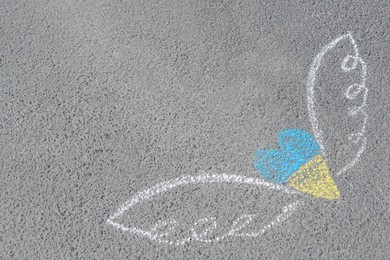 Photo of Heart and wings drawn with blue and yellow chalks on asphalt outdoors. Space for text